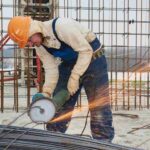 Worker using a handheld grinder to cut steel rebar, producing sparks at an active construction site.